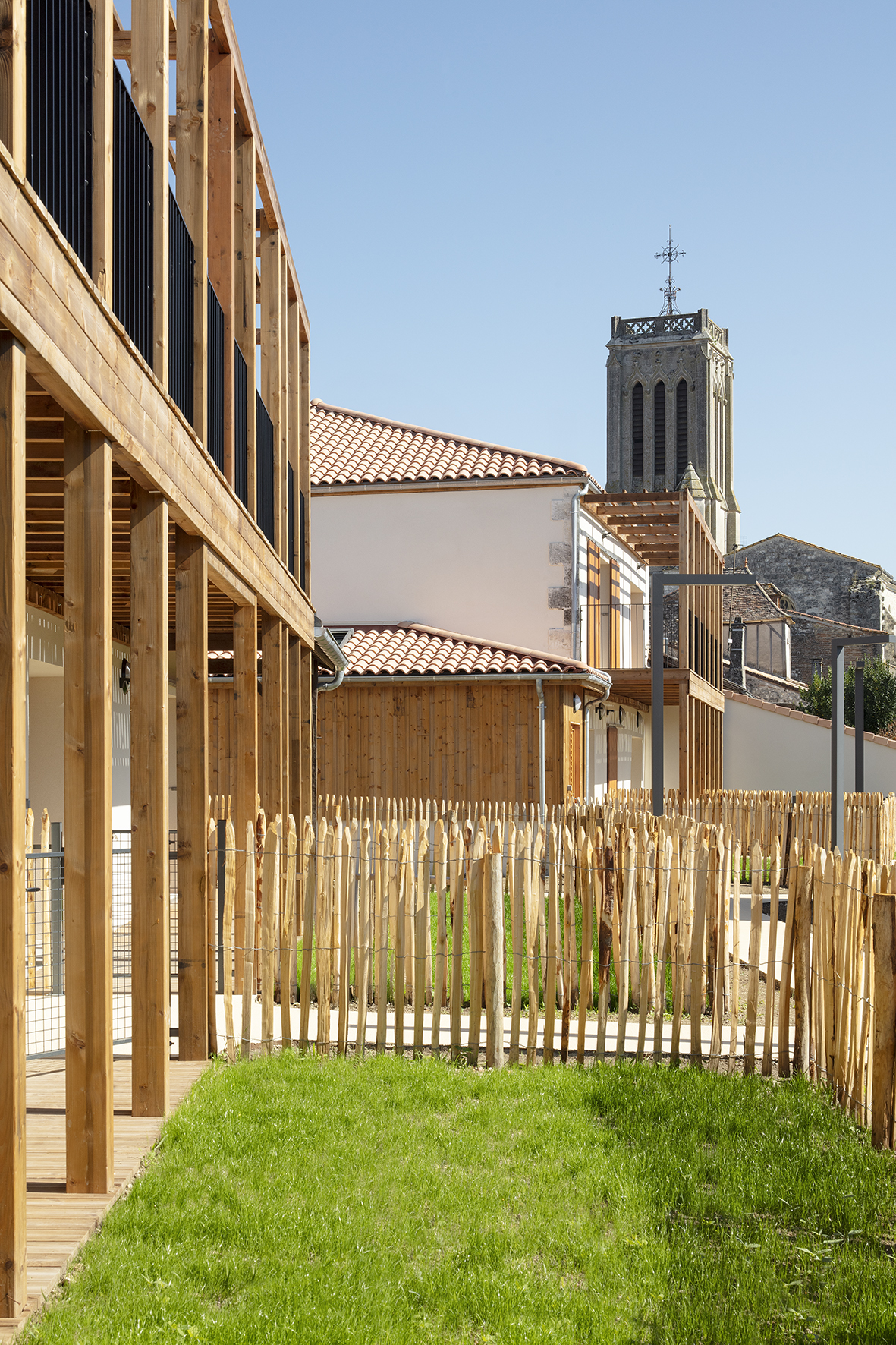 Cadrage sur l'église depuis les jardins / Agnès Clotis - Besson Bolze - Logements séniors et maison commune à la Sauvetat-du-Dropt - 01 octobre 2025