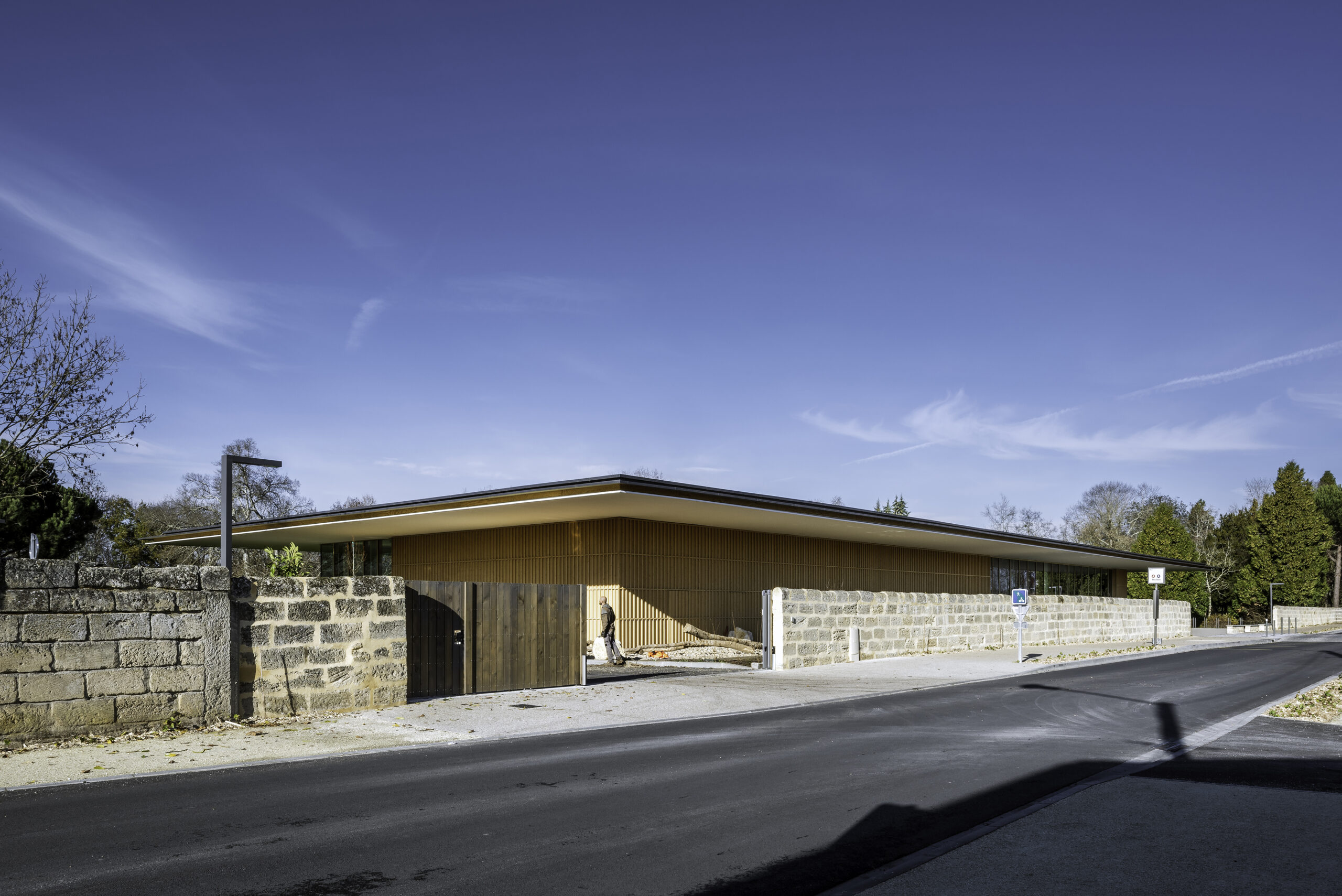 implanté le long du mur d'enceinte ne pierre du domaine, le bâtiment neuf joue le rôle d'élément signal maquant l'entrée du parc / Jean-François Tremege – Marjan Hessamfar et Joe Vérons architectes – Pôle culturel et festif BOMA, Saint-Denis-de-Pile, 2021