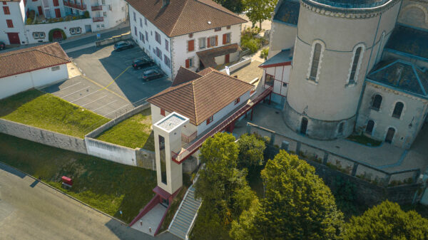 Trait d'union - Vue aérienne de l’aménagement d’accessibilité du centre-ville : ascenseur public et passerelle piétonne reliant l’esplanade de l’église aux espaces environnants. / Arthur Iscache - Prablanc Torres architecture -Accès cœur de ville – Création d’un ascenseur et d’une passerelle publics, Hasparren 64240, juillet 2025